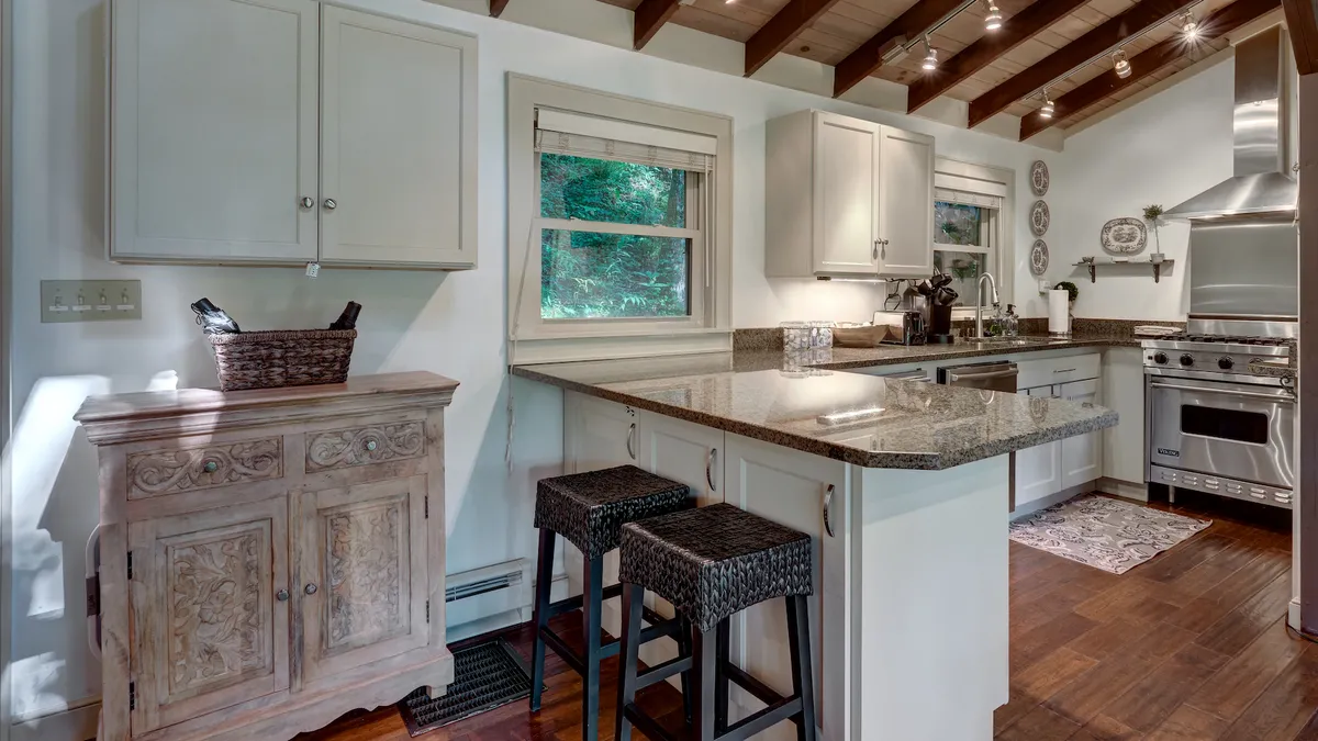 A cozy kitchen scene featuring a granite countertop island, wooden cabinetry, bar stools, and well-integrated kitchen appliances. Natural light streams in through the windows, illuminating the heart of the home where cooking and entertaining converge.