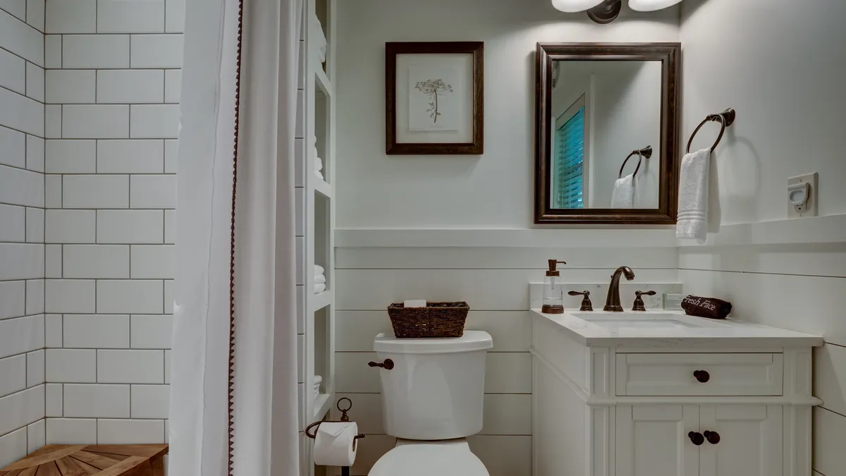 This image captures a tranquil bathroom with a vanity sink, framed artwork, a toilet, and a wooden stool, all set in a spa-like atmosphere. The space feels calm, promoting relaxation and solitude, hinting at the comfort and renewal guests can experience after an adventurous day outdoors.