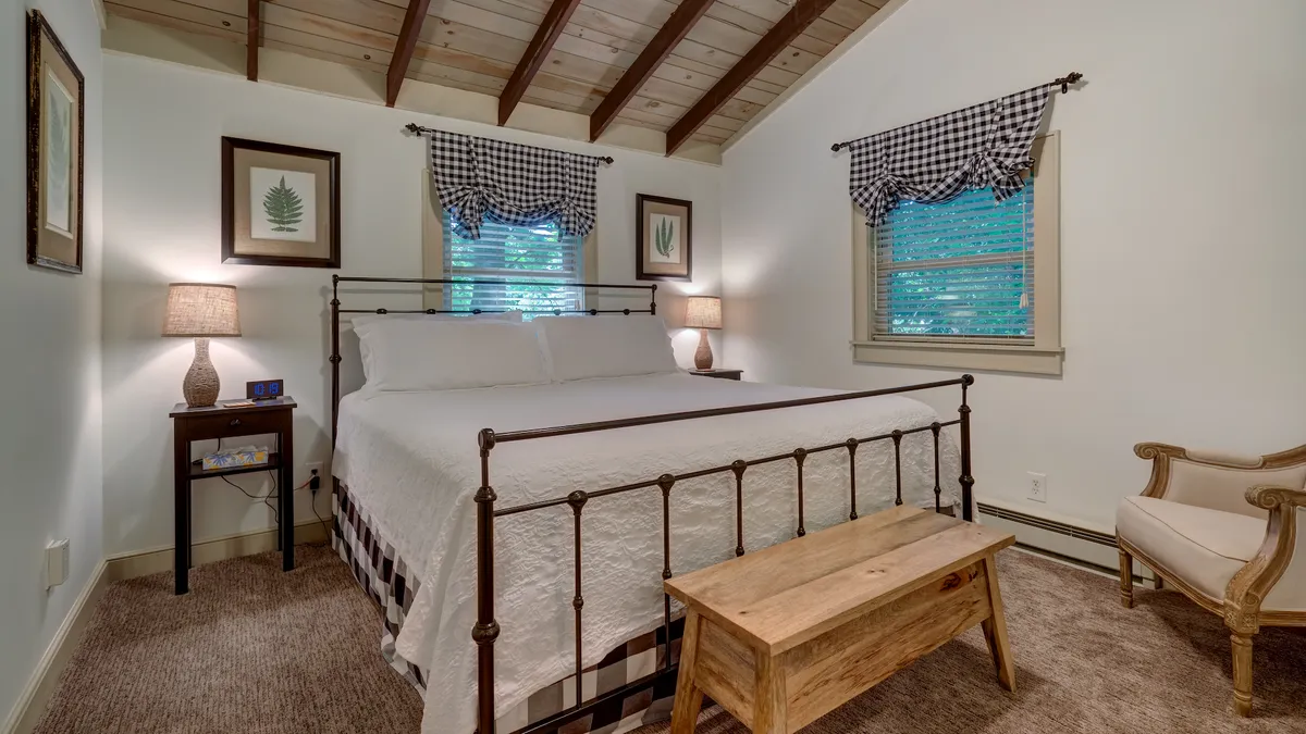 A cozy king bedroom featuring a neatly made bed with warm blankets, nightstands topped with lamps, decorative wall art, and a pair of chairs for relaxation. The room is awash with soft, natural light, reinforcing a soothing and inviting retreat.